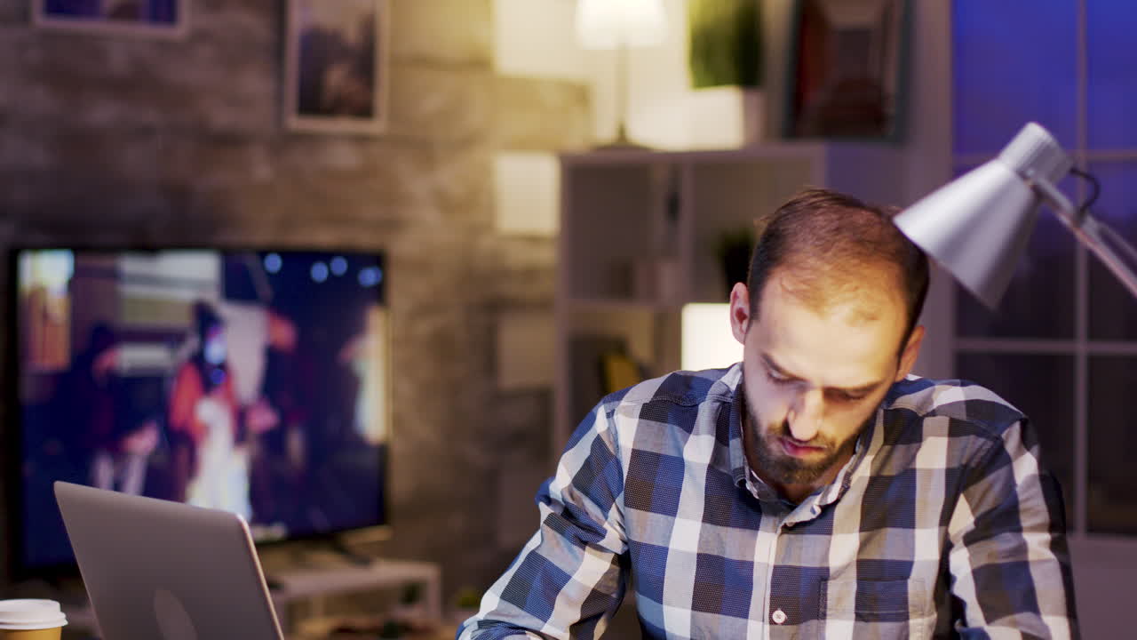 Man working on a laptop and writing on paper at his desk