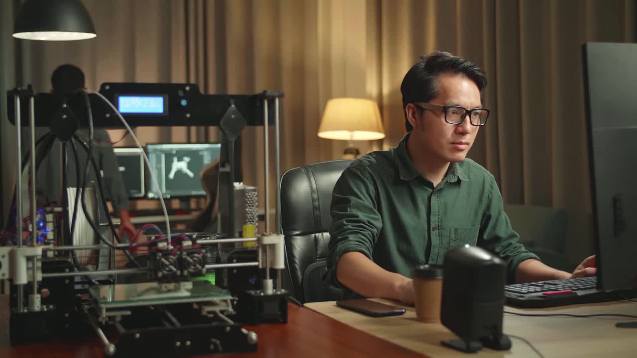 Asian Man Works On Personal Computer And 3D Printer In Home Office, He Works At Night