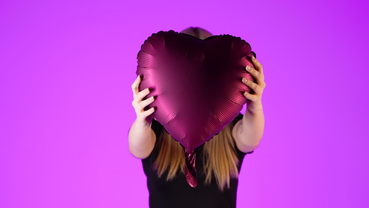 심장 모양의 보라색 풍선을 들고 있는 예쁜 젊은 금발 여성, 다채로운 스튜디오 초상화