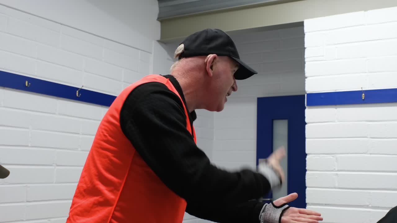 Coach motivating soccer team in locker room, wearing orange training vest