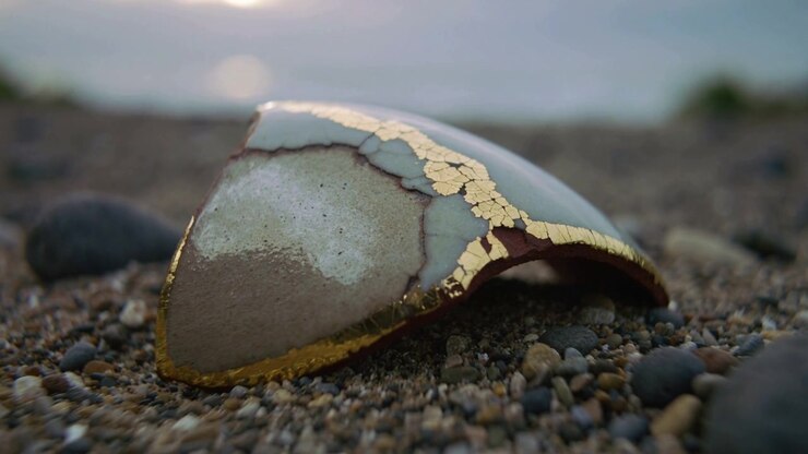 Pulling back camera as light shifting, highlighting mended shard on pebble shore with gold veins