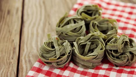 Roll-of-green-tagliatelle-pasta-with-red-and-white-checks-napkin-on-wooden-table-background