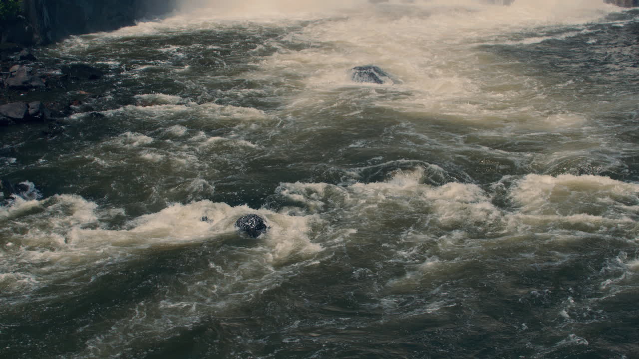 medium shot of bottom of new croton dam with powerful waterfall and stepped spillway leading down to the river. Tilt down following the flow of the river. Slow motion 40 fps