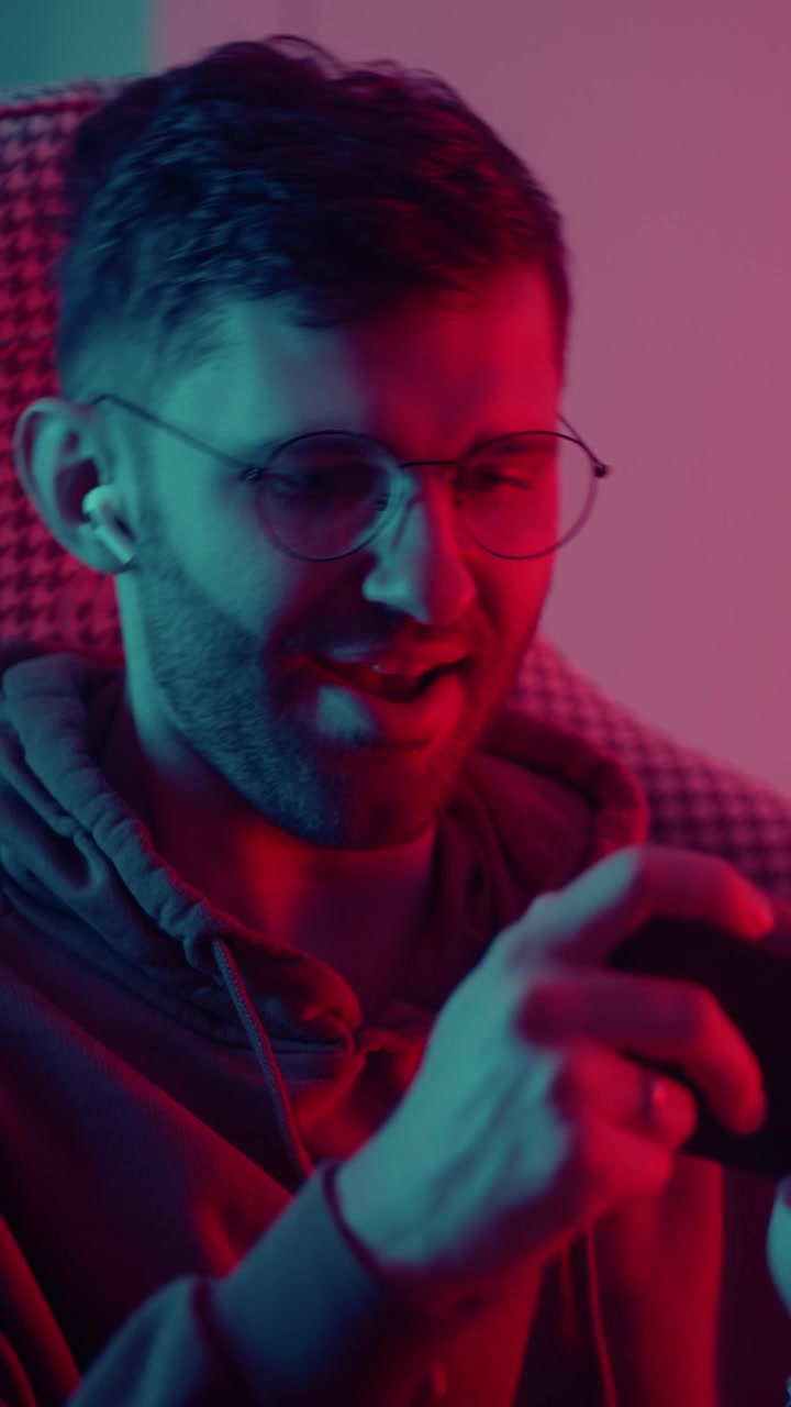 Giovane uomo entusiasta che gioca allo smartphone con luci al neon