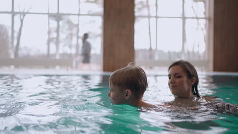 child boy is learning to swim in swimming pool with his mother family weekend in wellness center