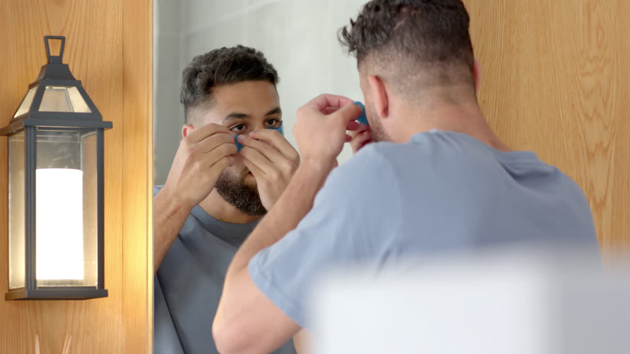 Man applying under eye patch in bathroom, focusing on skincare routine