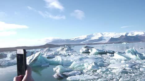 teléfono móvil tomando fotos de un lago con témpanos y montañas, islandia