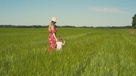 mother in red dress which flutters in the wind dressing hat walks along the endless field