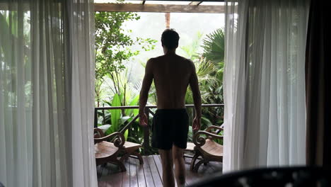 man walks from luxury bedroom to balcony surrounded by rain forest and fog