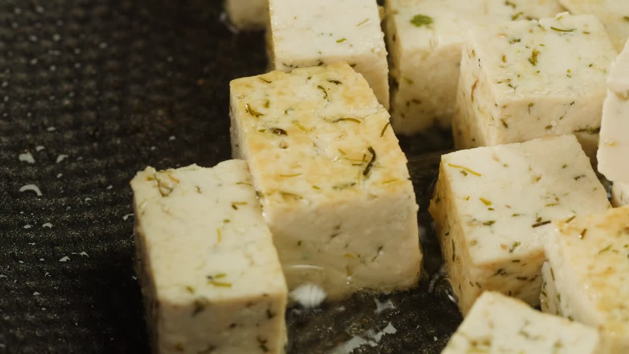 Fried tofu with sesame seeds and spices on cast iron pan, cooking japanese salad. Healthy ingredient for cooking vegan vegetarian diet food. Roasted tofu over black background.