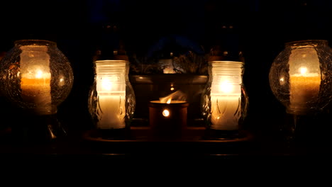 open air grave candle framed by glass lanterns at night on a cemetery tomb