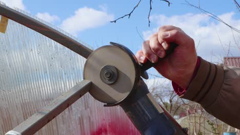 close-up of an angle grinder cutting an old metal greenhouse against a blue sky.