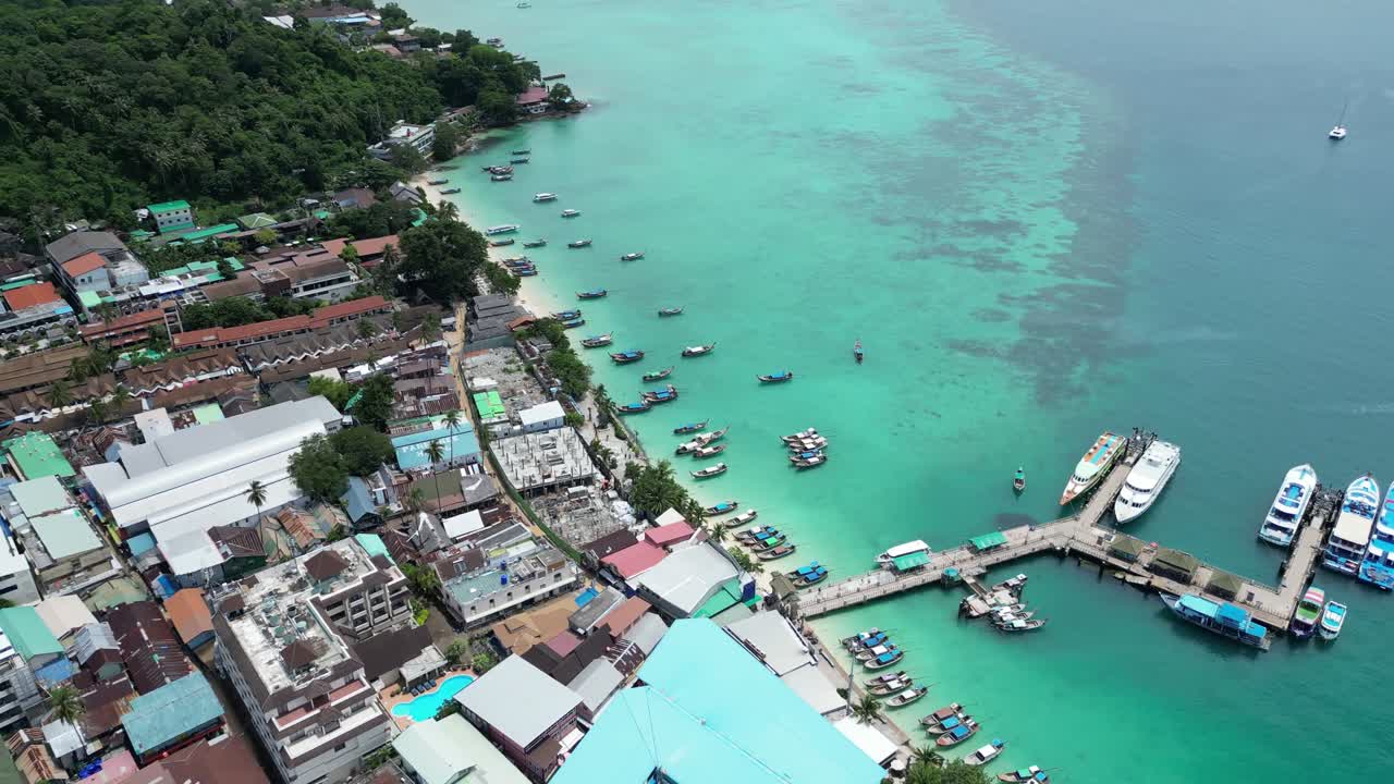 A partial aerial orbit capturing the bustling ferry terminal on Koh Phi Phi, Thailand, surrounded by vivid tropical waters.