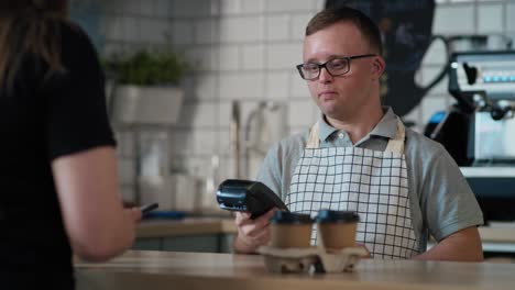 hombre caucásico con síndrome de down como camarero aceptando pagos sin contacto en el café.