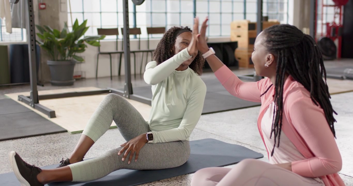 Amici africani in abbigliamento sportivo finiscono lo stretching in palestra, chiacchierano, ridono e si danno il cinque sui tappetini.