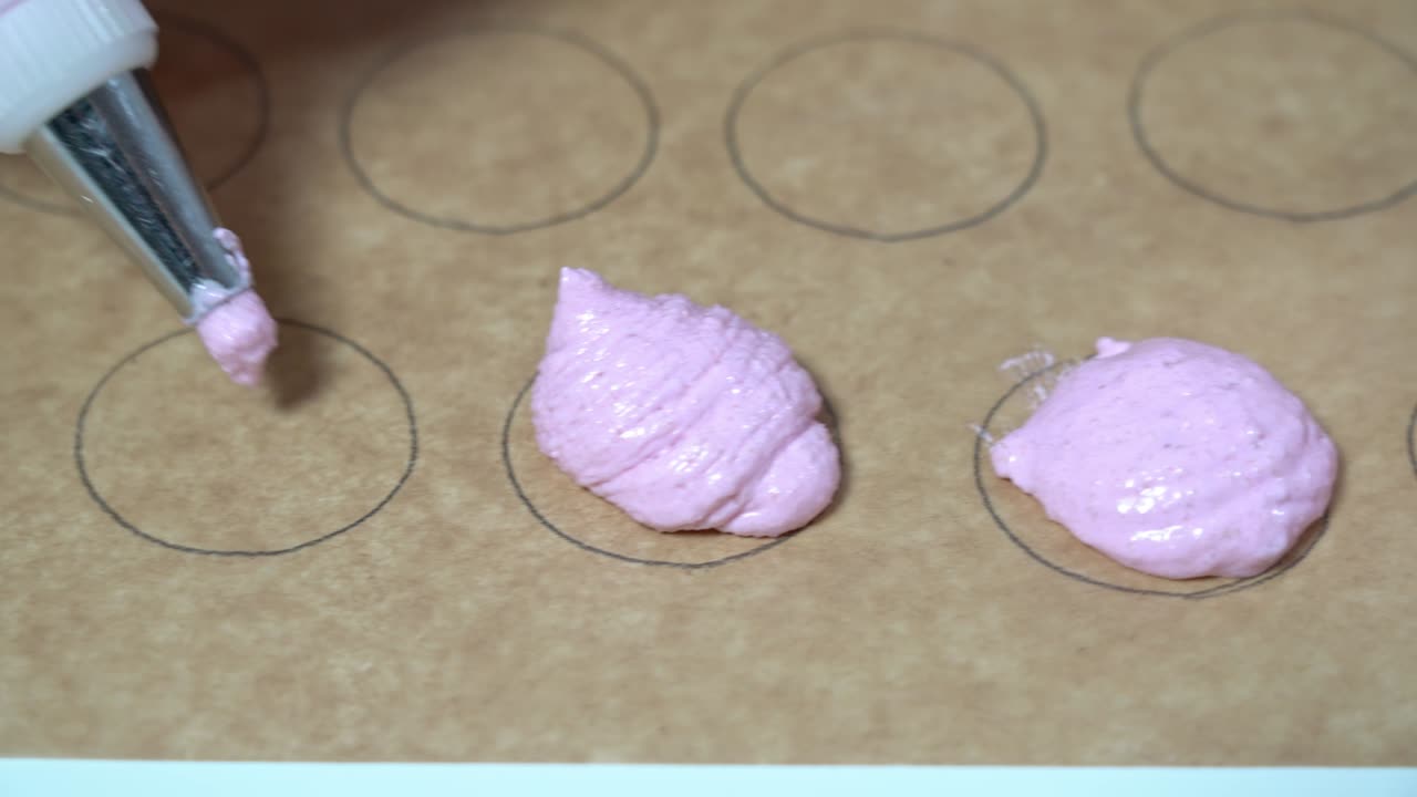 페르가멘트 종이에 원형 모양을 채우기 위해 마카론 분홍색 반죽으로 페이스트리 봉지를 사용하는 베이커의 근접 촬영.