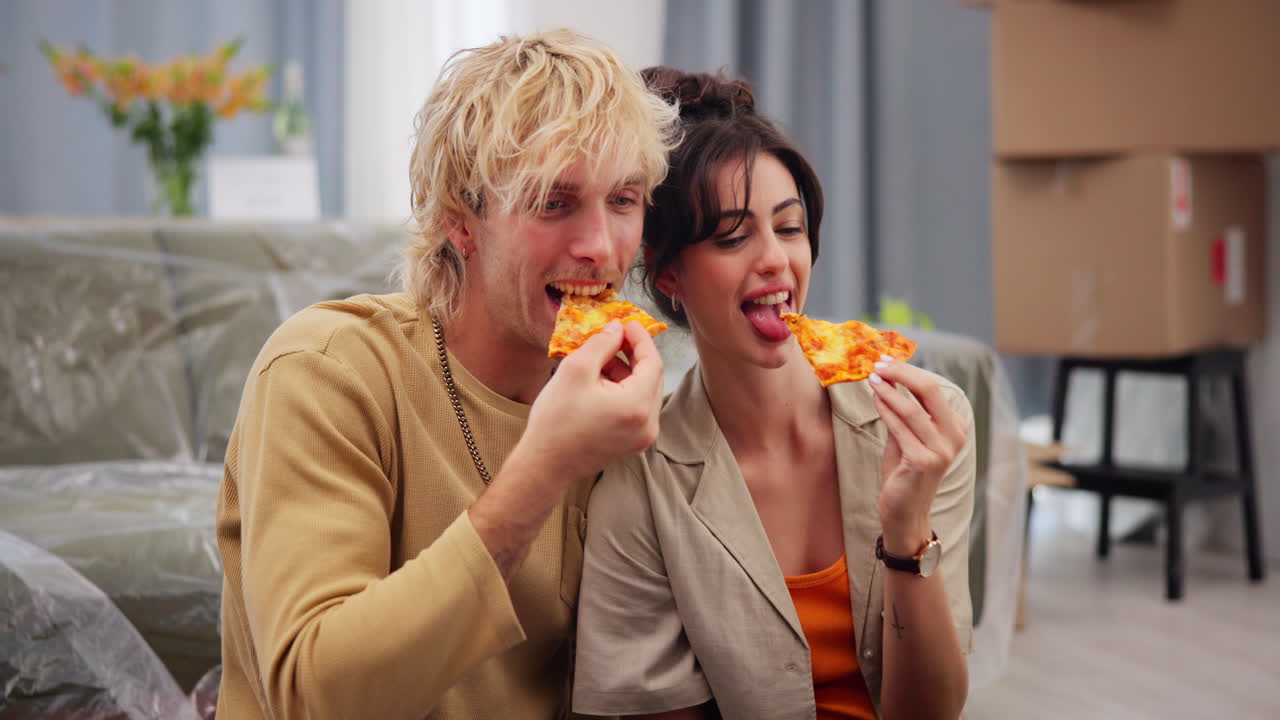 Coppia giovane che ride e mangia la pizza nella nuova casa
