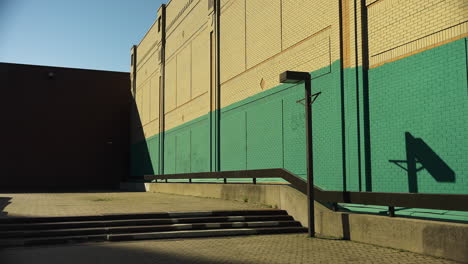 sunlit view of beige and teal brick wall with staircase, ramp and shadow casted by metal light pole. static shot