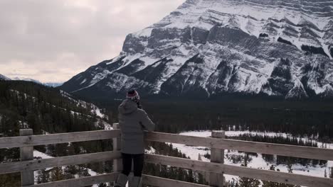 Young-Female-Hiker-Discovering-a-Stunning-Lookout-of-Mount-Rundle-in-Banff-Alberta-Canada,-Wide-Angle-Handheld-Tilt-Up-in-Winter-Daytime-Outside