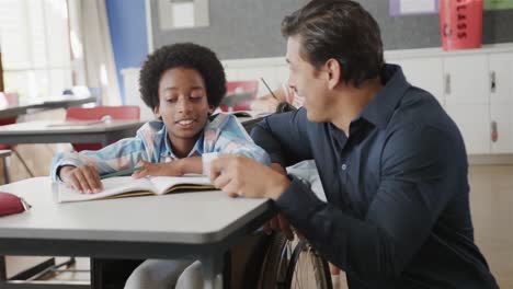 un maestro de sexo masculino feliz y un niño en silla de ruedas hablando en clase de escuela primaria, cámara lenta