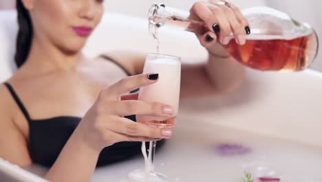 Pretty-young-woman-bathing-and-relaxing-with-glass-of-champagne-in-the-hot-tub-filled-with-milk-and-flowers.-Beautiful-woman