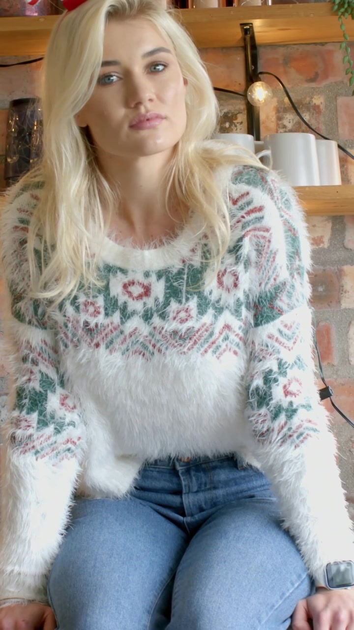 Vertikales Video: Kamera bemerkend, sich umdrehende Frau blickt nach vorne in einer Ziegelnische, Strickpullover, Uhr.