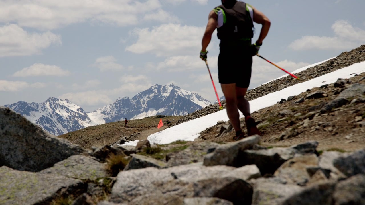 Un corridore con bastoncini da trekking si avvicina a una bandiera rossa lungo il sentiero alpino accidentato durante la Livigno Sky Marathon a Livigno, Italia - Piano medio.