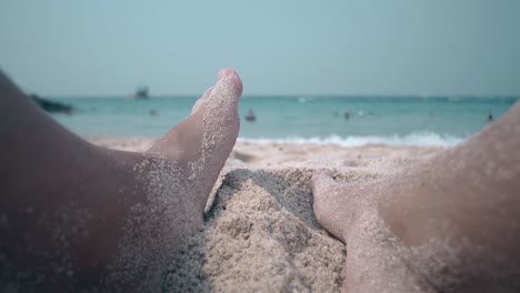 man buries feet in warm sand sitting on beach against ocean