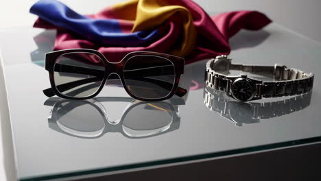 sunglasses, watch, and colorful scarf on reflective surface