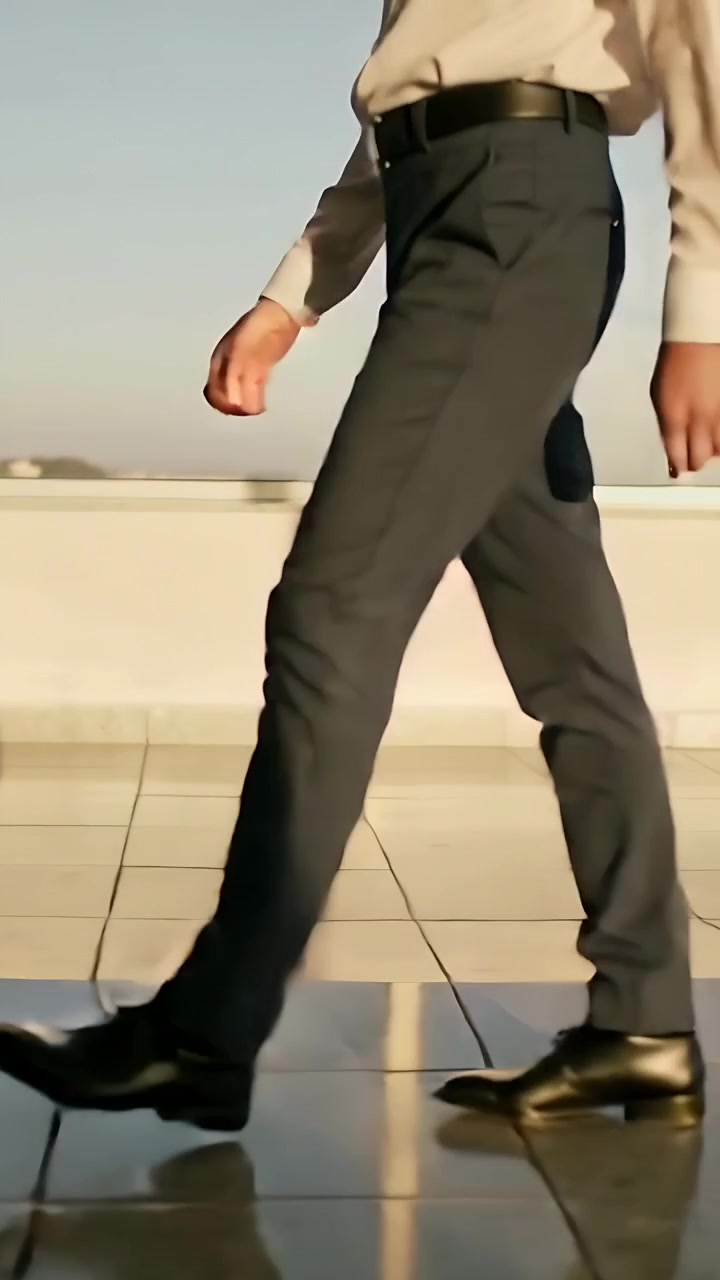 Dikey video: Gömlek ve pantolonlu bir adam sağdan girerek çatıyı geçiyor, ayakkabıları yansıyor.