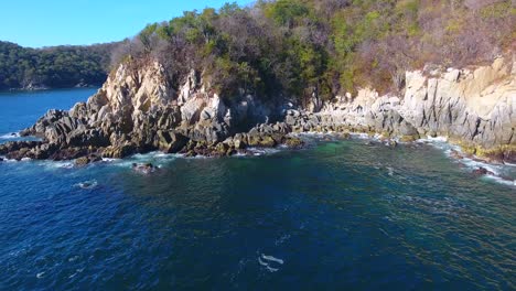 low angle strafe aerial of waves crashing on interesting coastal rock formations