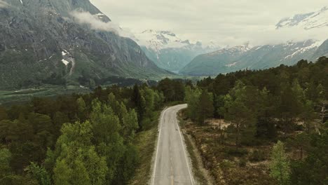 Iconic-forest-road-and-mountains-in-background-in-Norway,-aerial-view