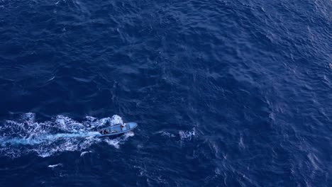 visión aérea de ángulo alto de un pequeño barco de pesca que se desplaza creando un lavado blanco en el océano rocoso