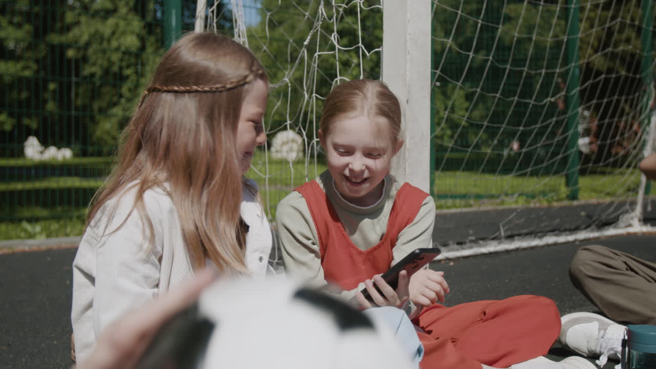 Happy young girls share a smartphone and laugh together on a sunny day