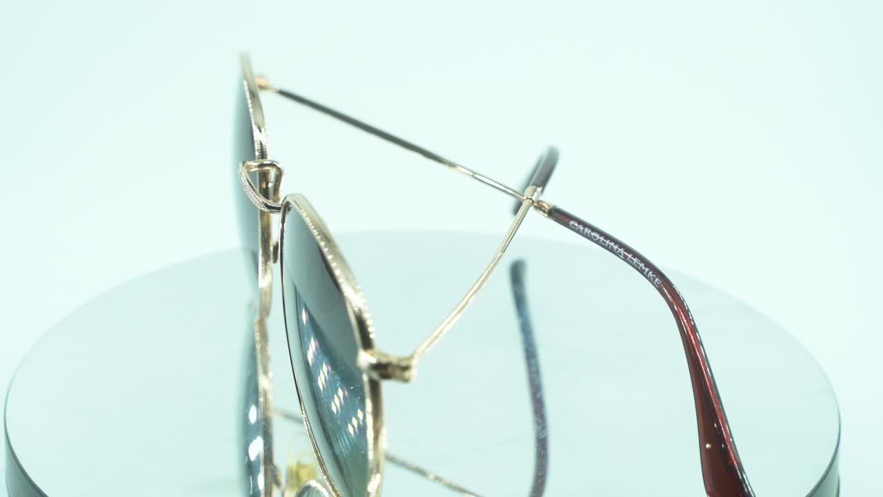 360도 회전 스탠드에 금색 선글라스를 놓는 클로즈업 샷, 그을린 유리, 스튜디오 조명, 제품 4k 비디오, 느린 동작