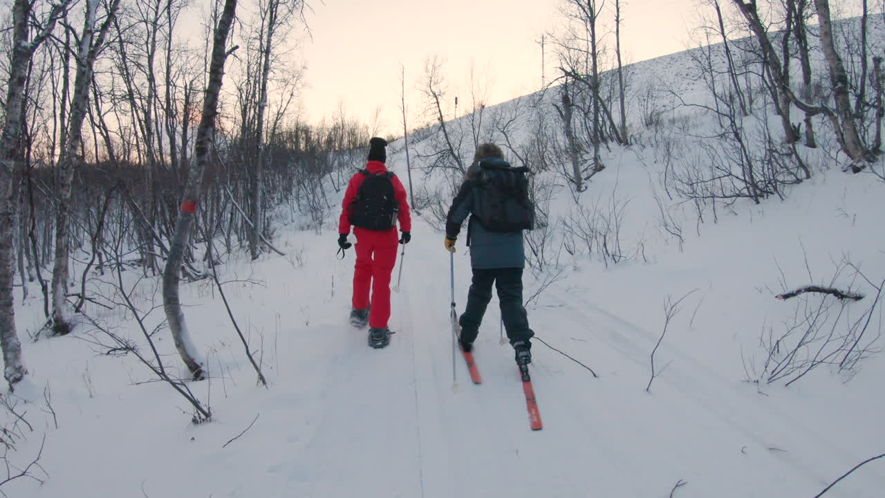 Male on cross country skis and a female on snowshoes hiking on a ski trail in the winter nature of Sweden.