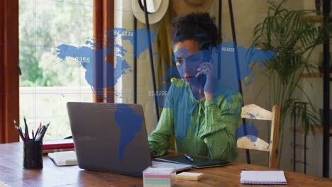 Animation-of-numbers,-map-over-biracial-woman-talking-on-cellphone-and-working-on-laptop-at-office
