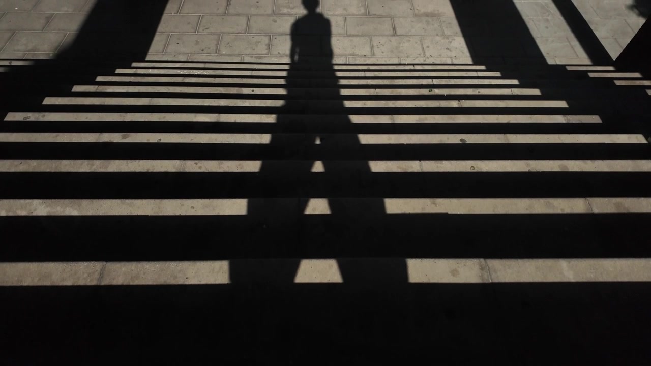 Dramatic shadow of a lone person cast on sunlit city stairs in Spain, creating bold geometric patterns and a mysterious self portrait vibe in strong natural light and urban surroundings.