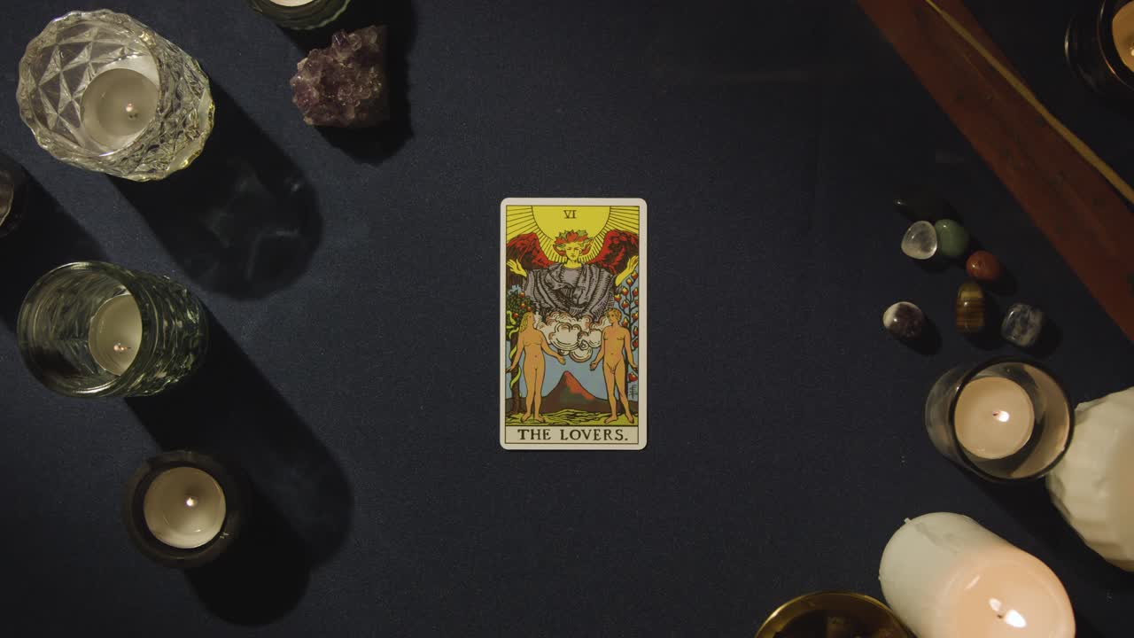 toma aérea de una persona que da una lectura de cartas del tarot colocando la carta de los amantes en la mesa