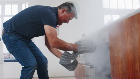 hombre maduro en la cocina toma la comida ardiendo del horno