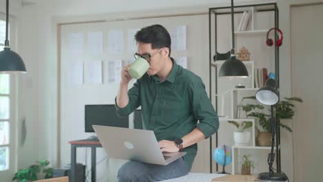 creative designer sits on his desk holds laptop on the knees drinks coffee while working on the project. creative designe and gaming content development studio