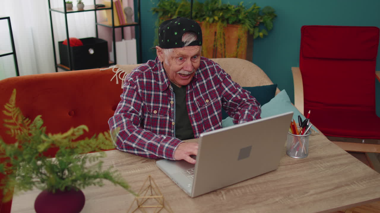 Grandfather man playing computer video games on laptop computer, wins, celebrate, smiles happily