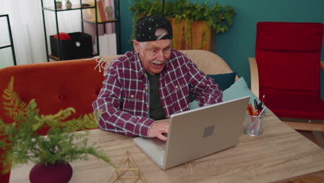 grandfather man playing computer video games on laptop computer, wins, celebrate, smiles happily