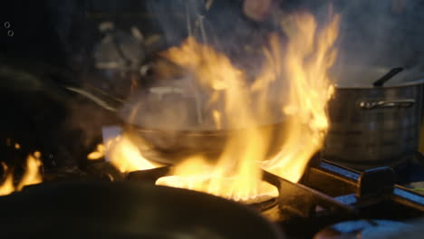 männlicher koch, der gemüse an der feuerflamme bratet