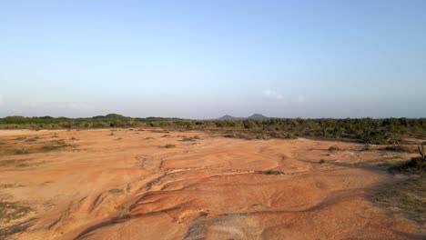 barren desert-like dry land revealed by the drone as it is flying in low altitude towards a grassland, forest, and mountains in the horizon, porlamar, margarita island, venezuela