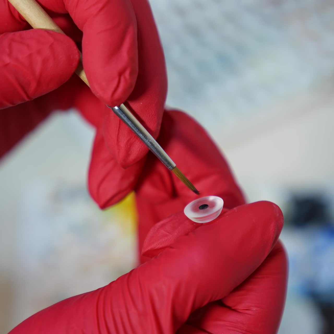 Making eye prosthesis in laboratory. Professional artist in medical gloves painting artificial eye with a brush. Ophthalmology concept. Close-up