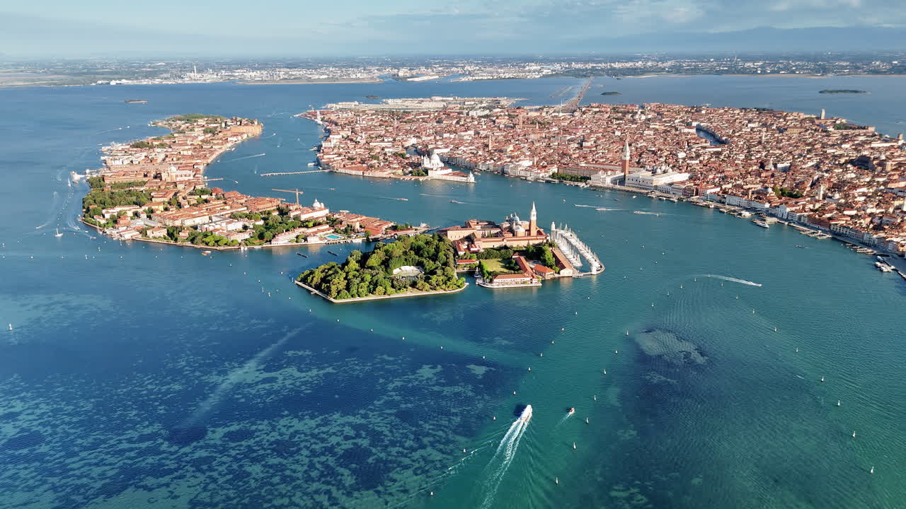Aerial drone view of the Venice Lagoon with San Giorgio Maggiore island and St. Mark's Basin. Boats move through turquoise water while the historic skyline of Venice spreads across the horizon