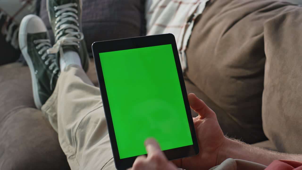 Online worker touching mockup tablet at home sofa closeup. Man choosing internet