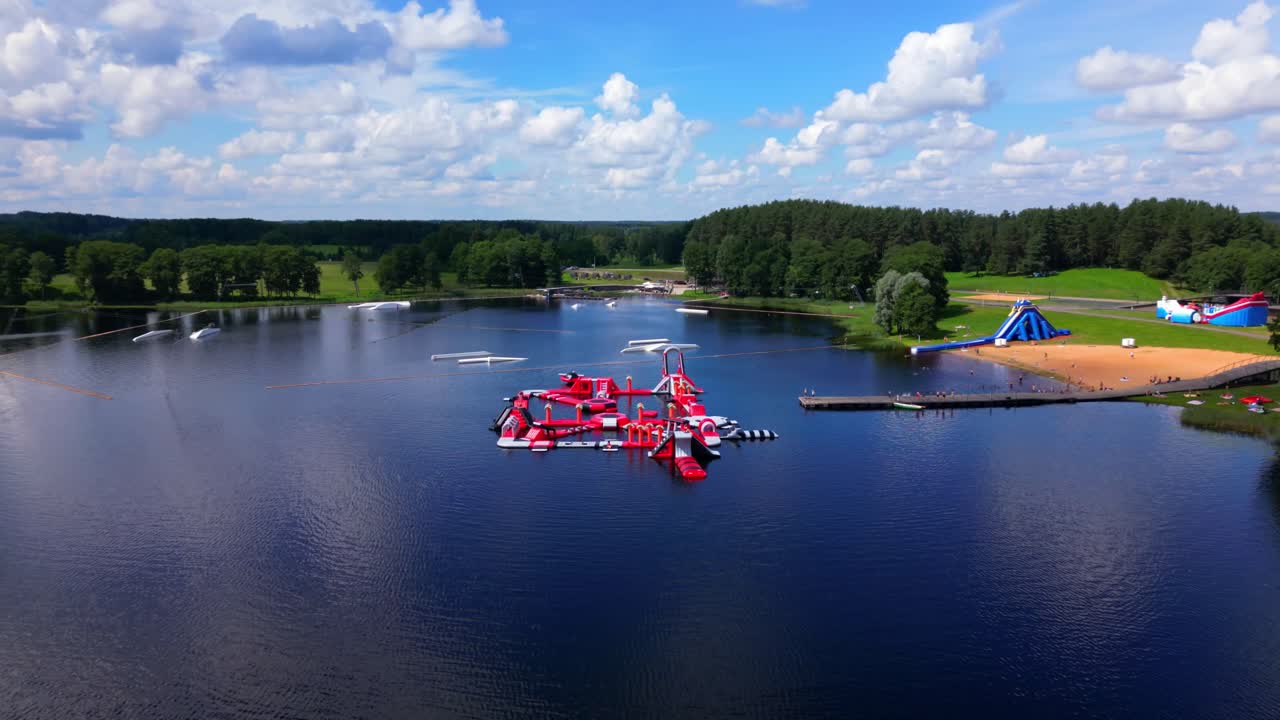 Aerial shot of inflatable lake park and sandy beach in Zarasai, surrounded by trees and open fields. Shot in Zarasai, Lithuania (Zarasai, Lietuva)