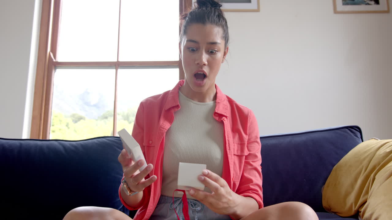 una adolescente biracial tiene una llamada de video sorprendida abriendo un regalo en casa, en cámara lenta.